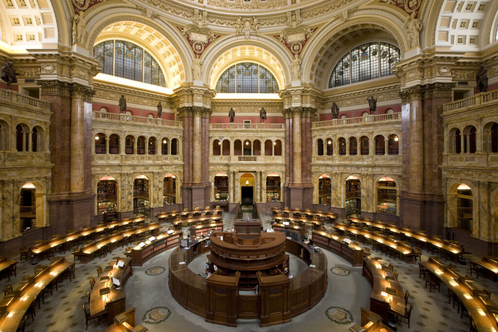 Wide interior view of the Library of Congress Main Reading Room with concentric desks beneath ornate arches.