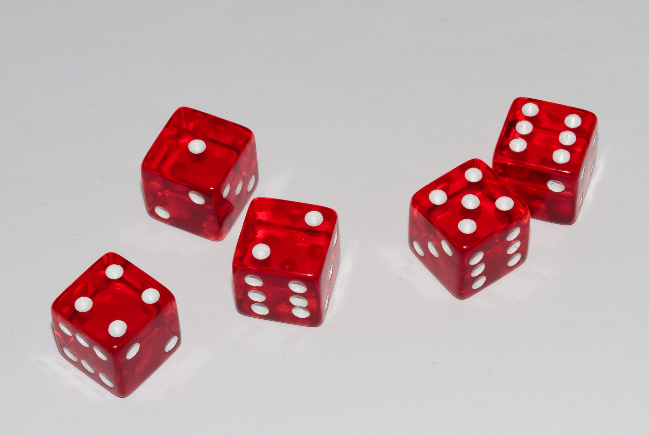 Five translucent red six-sided dice scattered across a pale surface.