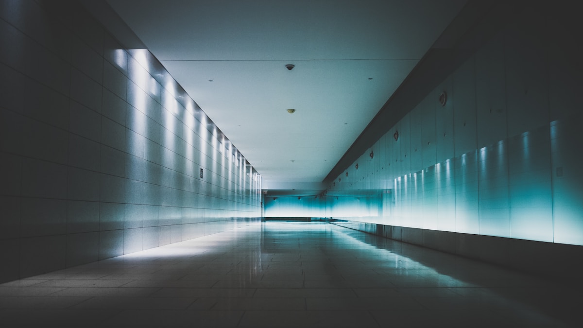 A symmetrical underground corridor lit blue, receding towards a bright doorway in Montreal.